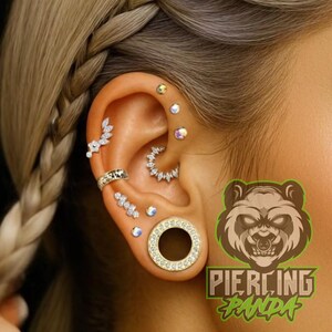 May include: Close-up of an ear adorned with various piercings, including a large gold tunnel and multiple small, sparkling studs. The ear also features a silver ring and a decorative, curved earring. The image includes the text "Piercing Panda" with a bear logo.