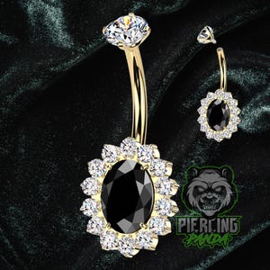 Op de afbeelding: Goudkleurige navelring met een grote zwarte ovale middensteen omringd door heldere kristallen. De bovenste steen is een heldere, druppelvormige kristal. Een kleinere, bijpassende ring is ook afgebeeld.