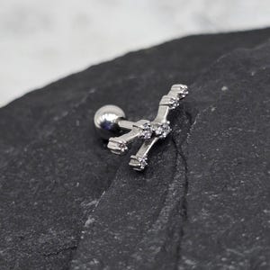 May include: Silver body piercing with a small ball on one end and a curved bar with five clear stones on the other end.