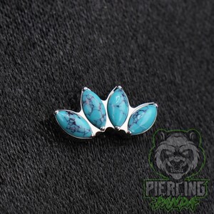 May include: A silver-toned body jewelry piece featuring four marquise-cut turquoise stones with dark veining arranged in a fan-like cluster. The stones are set in a metallic frame that curves slightly, creating a symmetrical, multi-stone design.