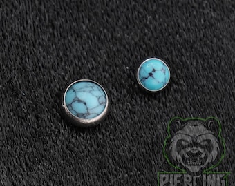 May include: Two round body jewelry pieces featuring smooth, light blue turquoise-colored stones with dark, web-like veining. Each stone is set within a simple, polished silver-toned metal bezel, creating a clean and circular profile for each item.