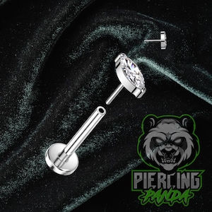 Puede incluir: Un piercing labret plateado con una gema transparente en forma de lágrima. El piercing se muestra desmontado, con el poste y la gema por separado. La imagen incluye el logotipo "Piercing Panda" en verde y blanco.