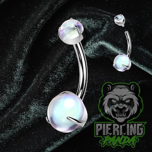 Pode incluir: Um piercing de umbigo prateado com uma barra curva. Possui uma gema redonda, iridescente e grande na parte inferior e outra menor na parte superior, presas por quatro garras. Um anel menor e separado também é visível. O texto "Piercing Panda" também está presente.