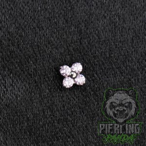 May include: A flower-shaped body jewelry stud featuring four round, clear, faceted stones arranged as petals around a central dark metallic bead. The piece has a polished silver-tone metal setting and is designed for piercing applications.