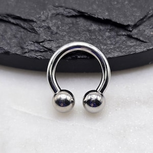 May include: A silver horseshoe barbell with two round balls on the ends. The barbell is on a white surface.
