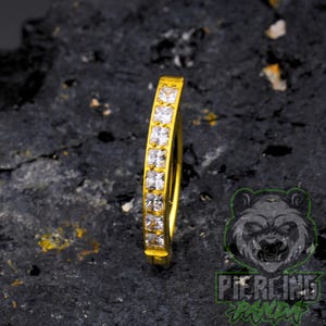 Piercing de umbigo em titânio dourado 14g com zircônias cúbicas cravejadas em formato quadrado e fecho de pressão.