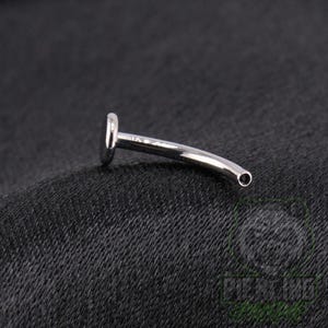 May include: A silver-colored curved barbell body jewelry piece featuring a flat circular disc at one end and a hollow opening at the other. The metal surface is smooth and reflective, showcasing a polished finish throughout the entire curved bar.