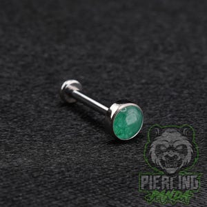 May include: A silver-toned metal labret piercing stud featuring a flat circular back and a front-facing circular setting containing a smooth, mottled green stone. The jewelry piece has a straight post and a polished metallic finish throughout.