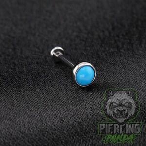May include: A silver-toned metal barbell body jewelry piece featuring a smooth, round, bright turquoise blue cabochon stone set at the end of a straight post. The jewelry has a polished metallic finish and a simple, clean, circular design.