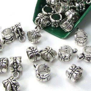May include: A close-up of silver-toned metal bead caps with a decorative design. The bead caps are scattered on a white surface and in a green scoop.
