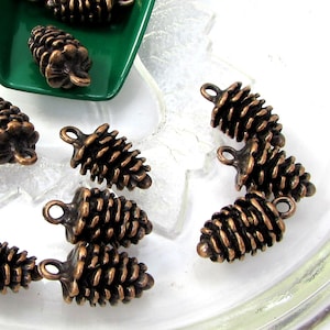 Puede incluir: Una colección de 12 abalorios de piña de pino de color cobre antiguo. Los abalorios son detallados y tienen un aspecto rústico. Son perfectos para añadir un toque de naturaleza a tus joyas o manualidades.