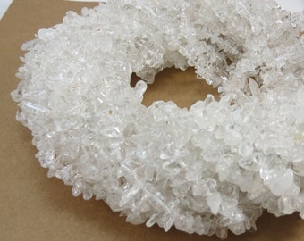 May include: A strand of clear quartz chips, arranged in a circle, on a brown background.