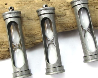 May include: Three silver-toned hourglass pendants with white sand. Each pendant is about 2 inches long and has a loop at the top for attaching to a chain or cord.