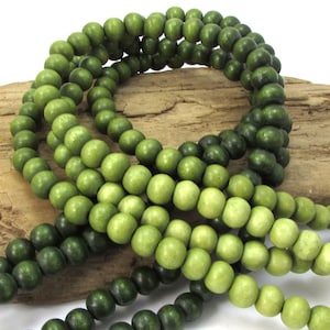 May include: A strand of green wooden beads with a gradient from dark green to light green. The beads are round and smooth.