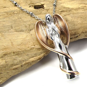 May include: A silver and rose gold angel pendant necklace. The angel is depicted with wings wrapped around its body and hands clasped in prayer. The pendant is attached to a silver chain.