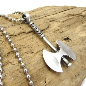 May include: A silver axe pendant necklace with a ball chain. The axe has a detailed handle and a double-headed blade.