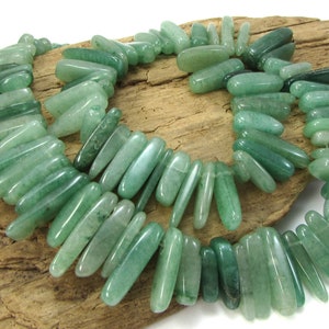May include: A strand of green jade beads, each bead is a long, thin, and slightly curved shape.