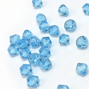 May include: A scattering of light blue crystal beads, each with a faceted design. The beads are arranged on a white surface.