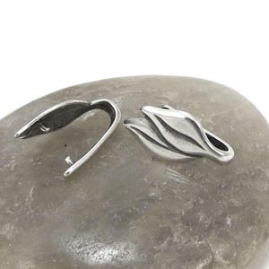 May include: Two silver-toned metal clasps for jewelry making. One clasp is a simple loop, the other is shaped like a leaf.