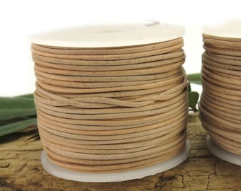 May include: Two spools of light brown leather cord, wound around white spools. The cord is thin and smooth.