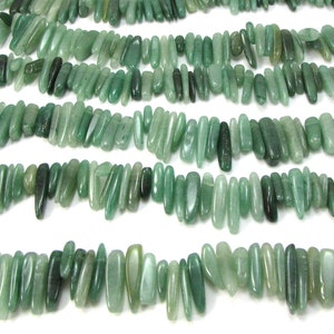 May include: A strand of light green gemstone beads, each bead is a long, thin, irregular shape. The beads are strung together to form a long necklace.