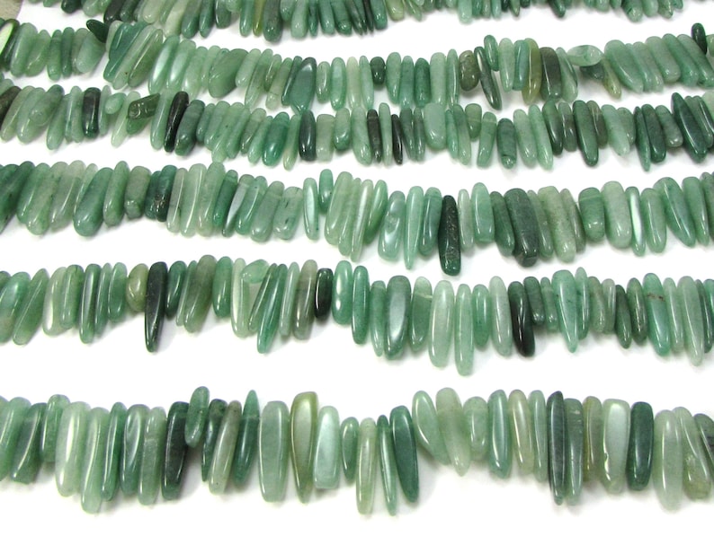 May include: A strand of light green gemstone beads, each bead is a long, thin, irregular shape. The beads are strung together to form a long necklace.