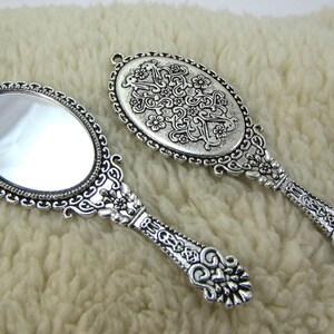 May include: Two ornate silver hand mirrors with intricate floral designs. One mirror has a clear reflective surface, while the other has a decorative design on the reflective surface.
