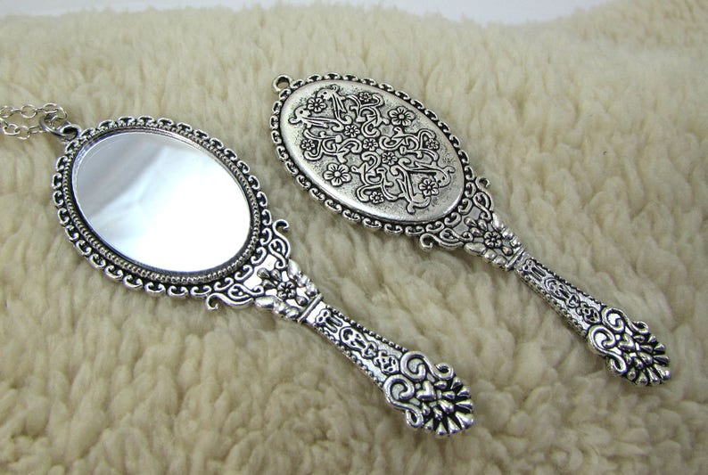 May include: Two ornate silver hand mirrors with intricate floral designs. One mirror has a clear reflective surface, while the other has a decorative design on the reflective surface.