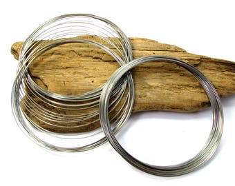 May include: A pile of silver-colored metal wire rings, stacked on a piece of driftwood. The rings are all the same size and are made of thin wire.