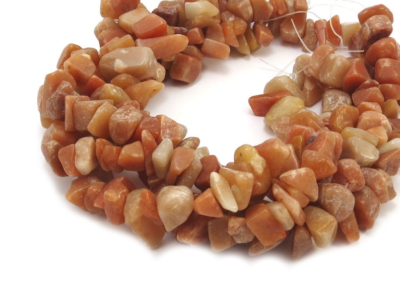 May include: A strand of orange and yellow chip-shaped gemstone beads. The beads are irregular in shape and size, and have a natural, rough texture.
