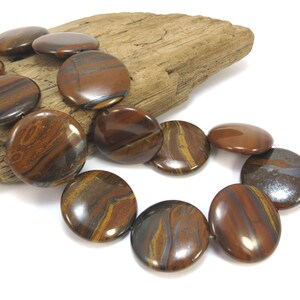May include: A strand of round, brown and gold tiger's eye beads with silver flecks. The beads are strung on a cord and are approximately 2.5 cm in diameter.