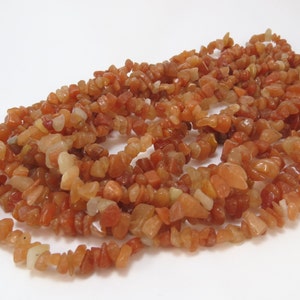 May include: A strand of carnelian chip beads. The beads are a mix of orange and red colors and have a natural, irregular shape.