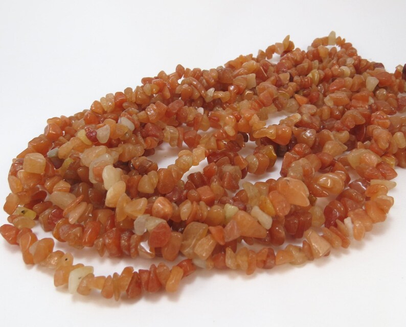 May include: A strand of carnelian chip beads. The beads are a mix of orange and red colors and have a natural, irregular shape.