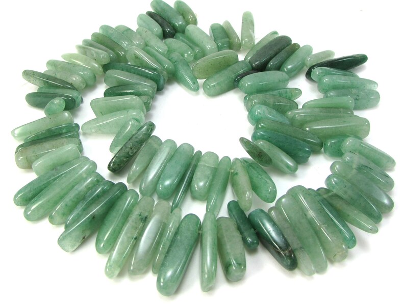 May include: A strand of green jade gemstone beads, each bead is a long, slender, and slightly irregular shape.