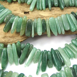 May include: A strand of green jade gemstone beads, each bead is a long, slender, and slightly pointed oval shape. The beads are strung together on a clear thread and are arranged in a staggered pattern.