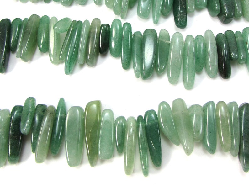 May include: A strand of light green, natural stone beads. The beads are long and narrow, with a slightly irregular shape. They are strung together on a clear thread.