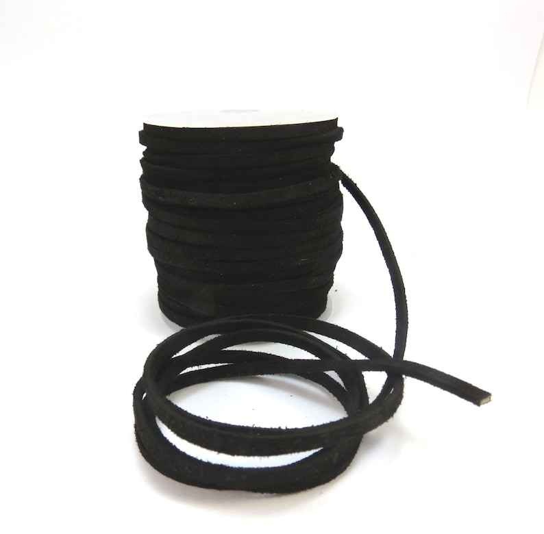 May include: A spool of black suede cord, approximately 3mm wide, is shown on a white background. The cord is wound around a white cardboard spool and a length of cord is hanging off the spool.