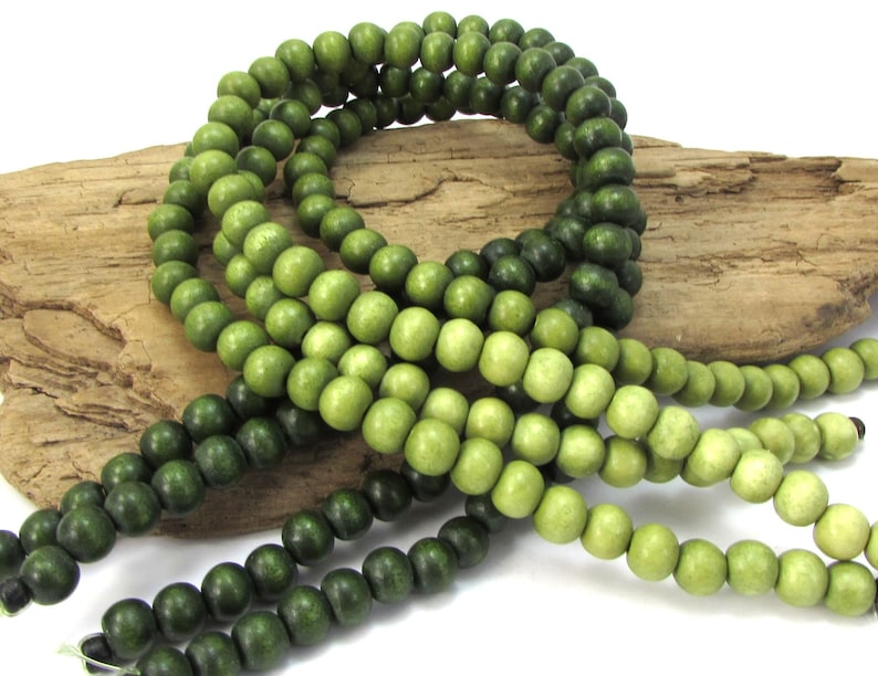 May include: A strand of green wooden beads with a gradient from dark green to light green. The beads are round and smooth.