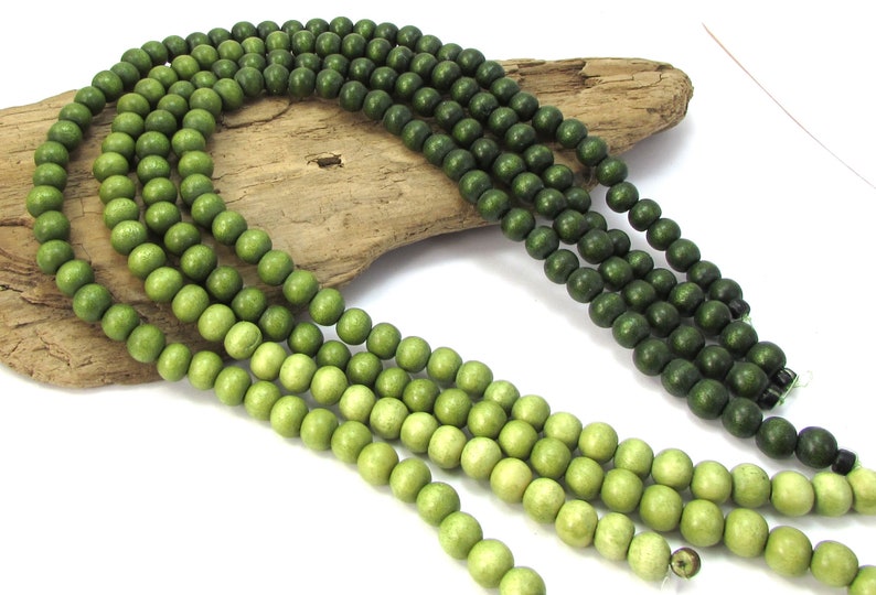 Peut inclure: Un brin de perles en bois dans des tons de vert, allant du vert clair au vert fonc&eacute;. Les perles sont rondes et lisses, et elles sont enfil&eacute;es sur un fil transparent.
