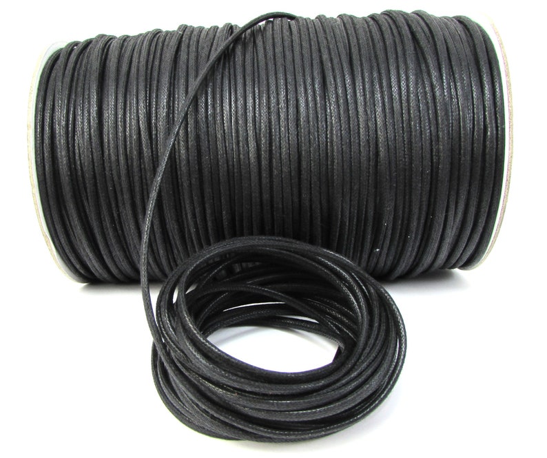 May include: A spool of black waxed cotton cord. The cord is wound tightly around the spool and is ready to be used for crafting projects.