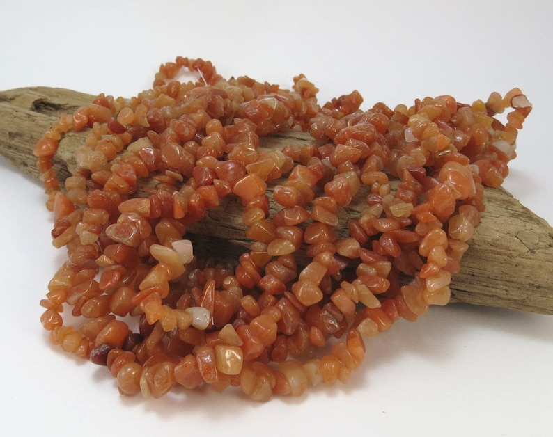 May include: A strand of carnelian chip beads in shades of orange and red. The beads are irregular in shape and size, and they are strung on a clear thread.