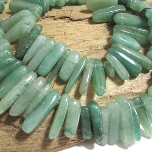 May include: A strand of light green jade beads, each bead is a long, slender, and slightly curved shape.