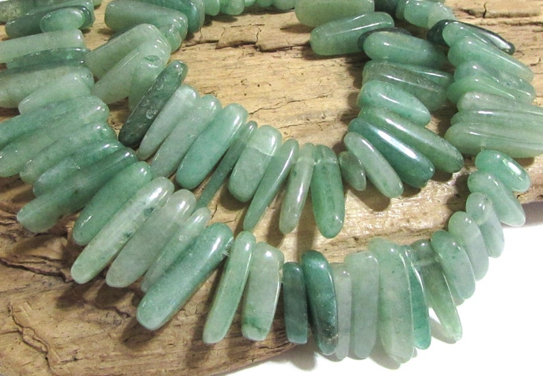 May include: A strand of light green jade beads, each bead is a long, slender, and slightly curved shape.