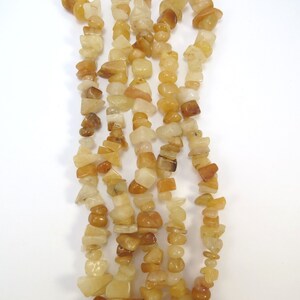 May include: A strand of yellow and orange gemstone beads. The beads are irregular in shape and size, and they are strung on a clear thread. The beads are all natural and have a polished finish.