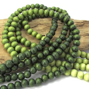 Peut inclure: Un brin de perles en bois dans des tons de vert, allant du clair au fonc&eacute;. Les perles sont rondes et lisses, et elles sont enfil&eacute;es sur un cordon.
