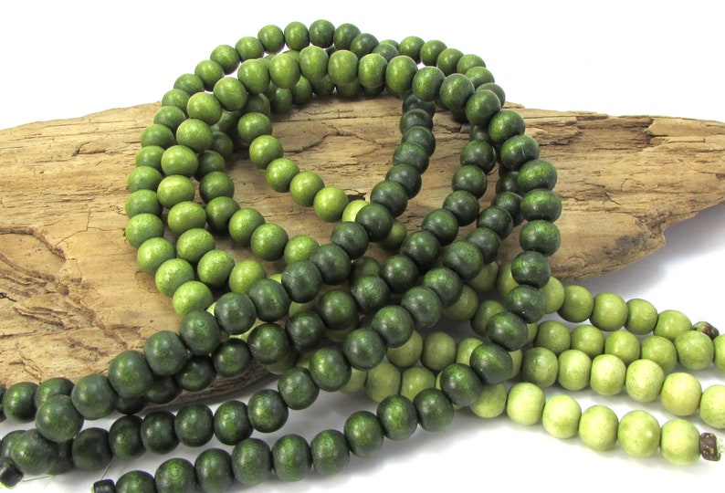 Peut inclure: Un brin de perles en bois dans des tons de vert, allant du clair au fonc&eacute;. Les perles sont rondes et lisses, et elles sont enfil&eacute;es sur un cordon.
