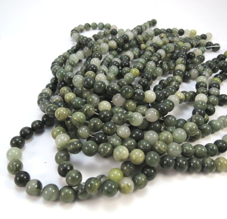 May include: A strand of green and white jade beads. The beads are round and have a smooth, polished finish. The beads are strung on a clear thread.
