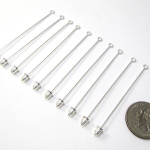 Puede incluir: Diez alfileres de cabeza plateados con un bucle en la parte superior y una peque&ntilde;a tapa plateada en la parte inferior. Los alfileres de cabeza miden aproximadamente 3,8 cm de largo y se muestran junto a una moneda de 20 c&eacute;ntimos de euro para comparar el tama&ntilde;o.
