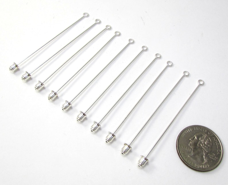 Puede incluir: Diez alfileres de cabeza plateados con un bucle en la parte superior y una peque&ntilde;a tapa plateada en la parte inferior. Los alfileres de cabeza miden aproximadamente 3,8 cm de largo y se muestran junto a una moneda de 20 c&eacute;ntimos de euro para comparar el tama&ntilde;o.
