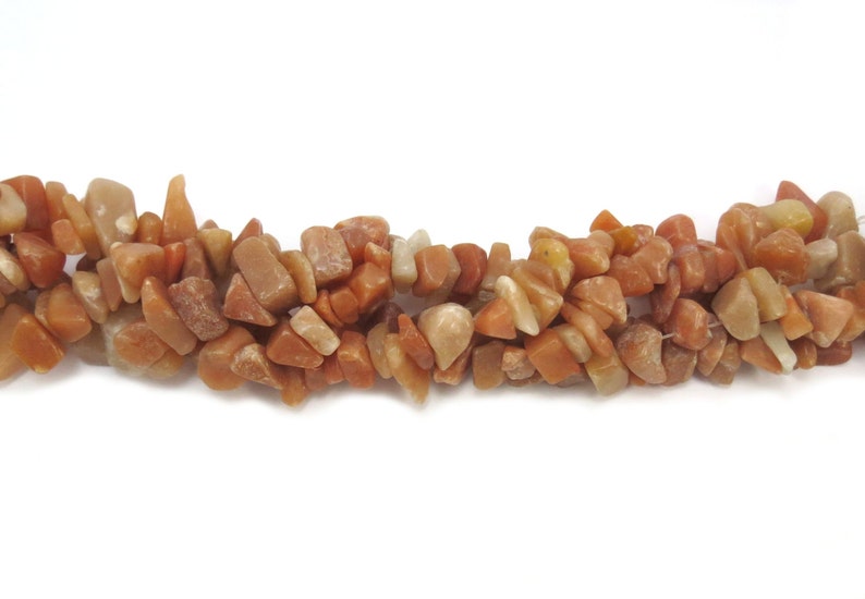 May include: A strand of chip-shaped carnelian gemstone beads. The beads are a mix of light and dark orange colors.